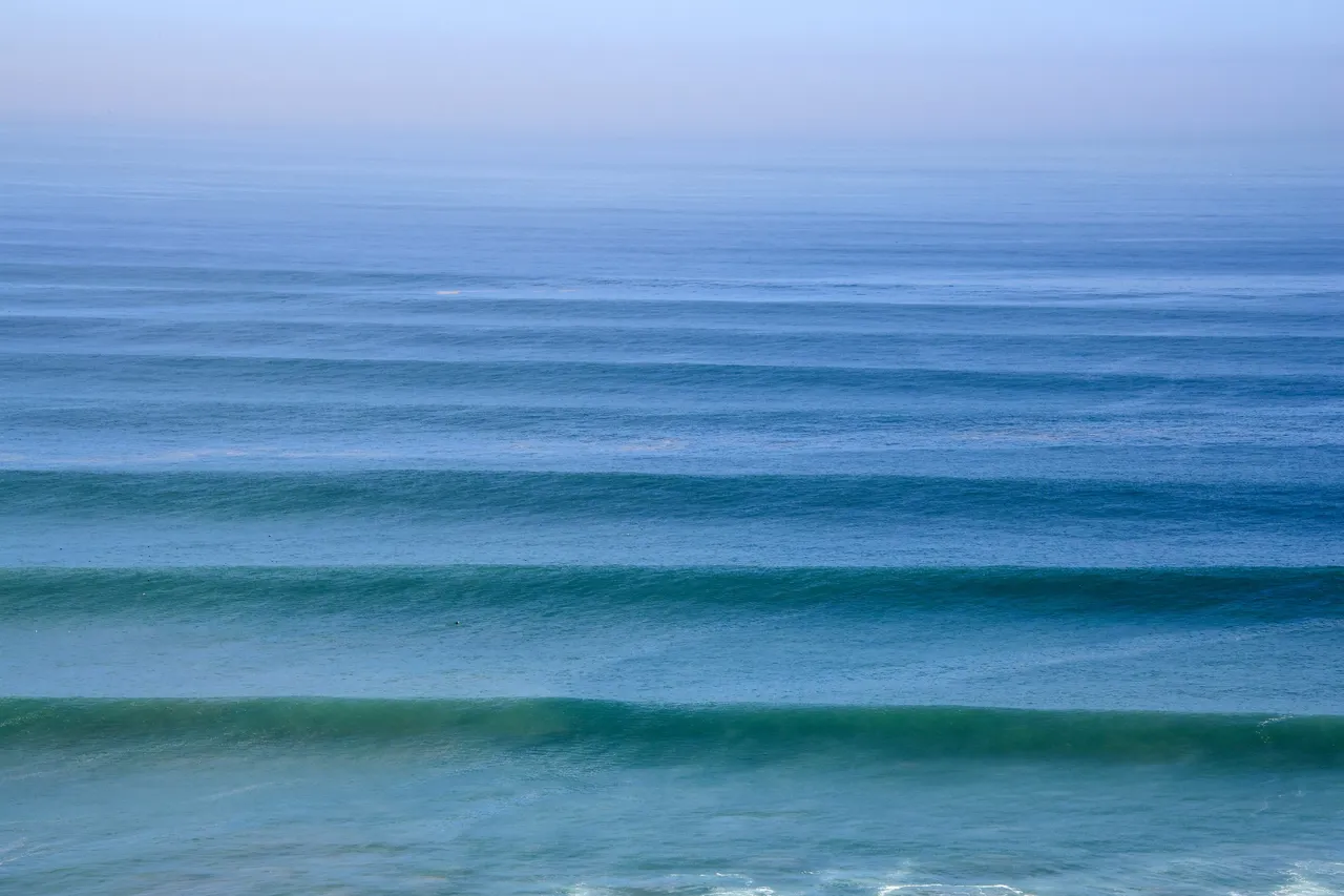 Long, even lines of swell moving across a blue ocean.