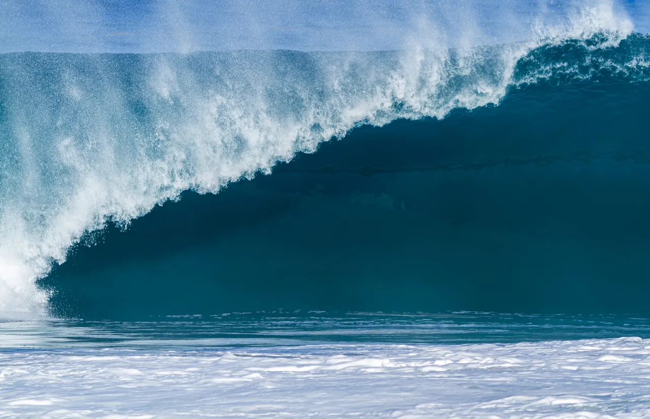 A deep blue wave curling over, with spray along its crest.