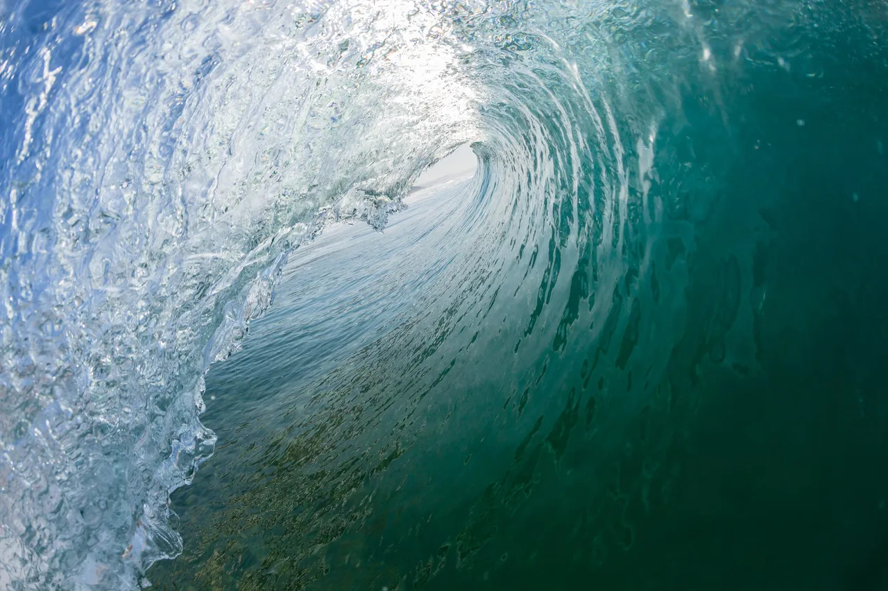 The inside of a breaking wave, clear water curving overhead.