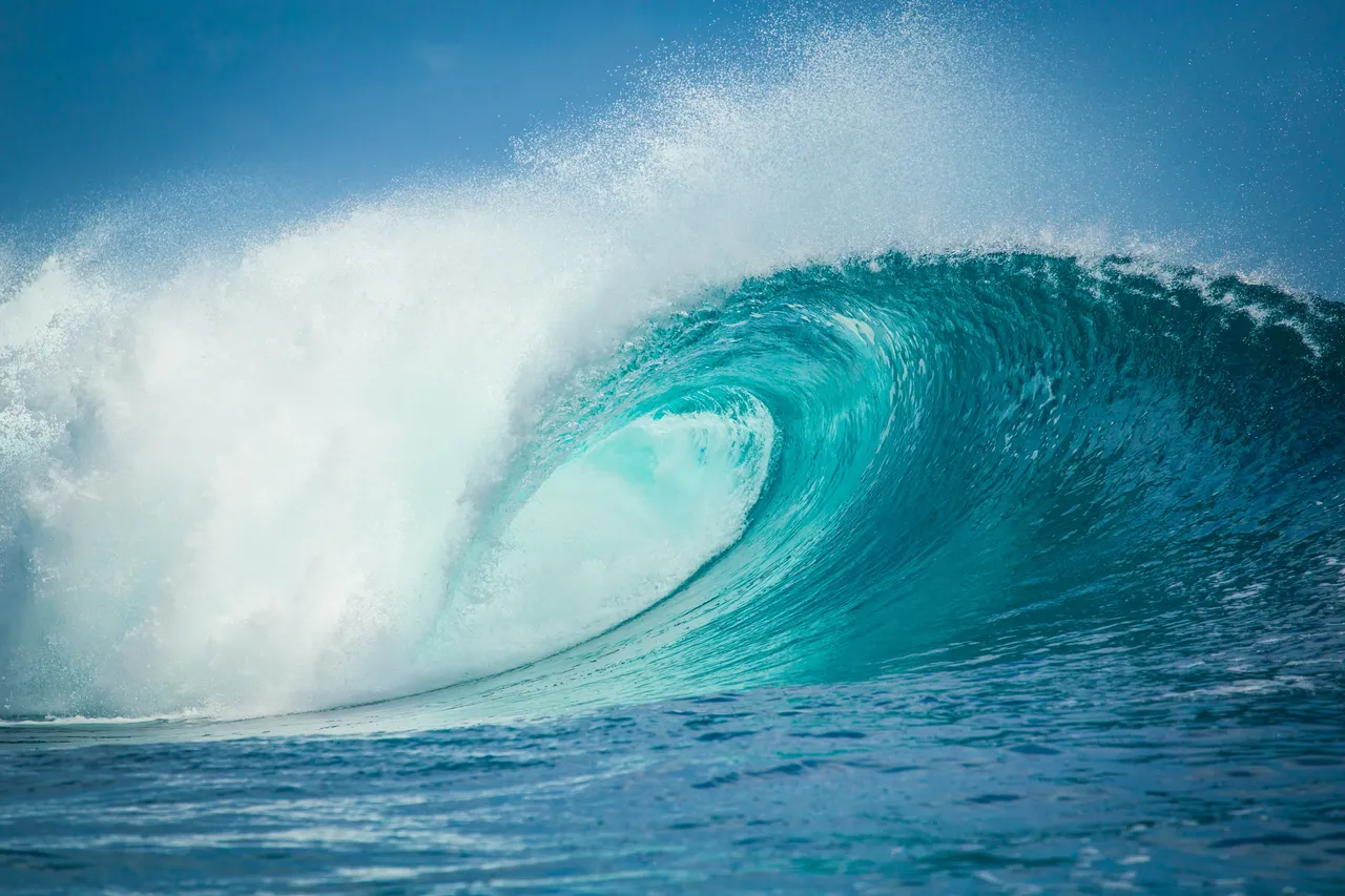 A turquoise wave curling into a hollow barrel, spray lifting off its crest.